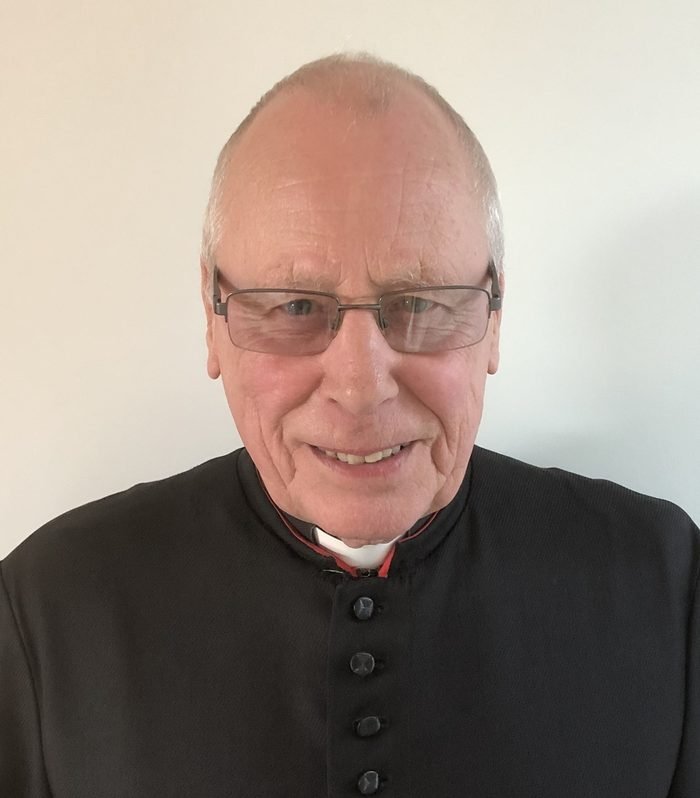 Fr Roger Caswell, in a black cassock, smiling.