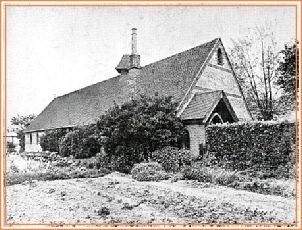 A black and white photograph of the original mission room, a long low building with a small porch.