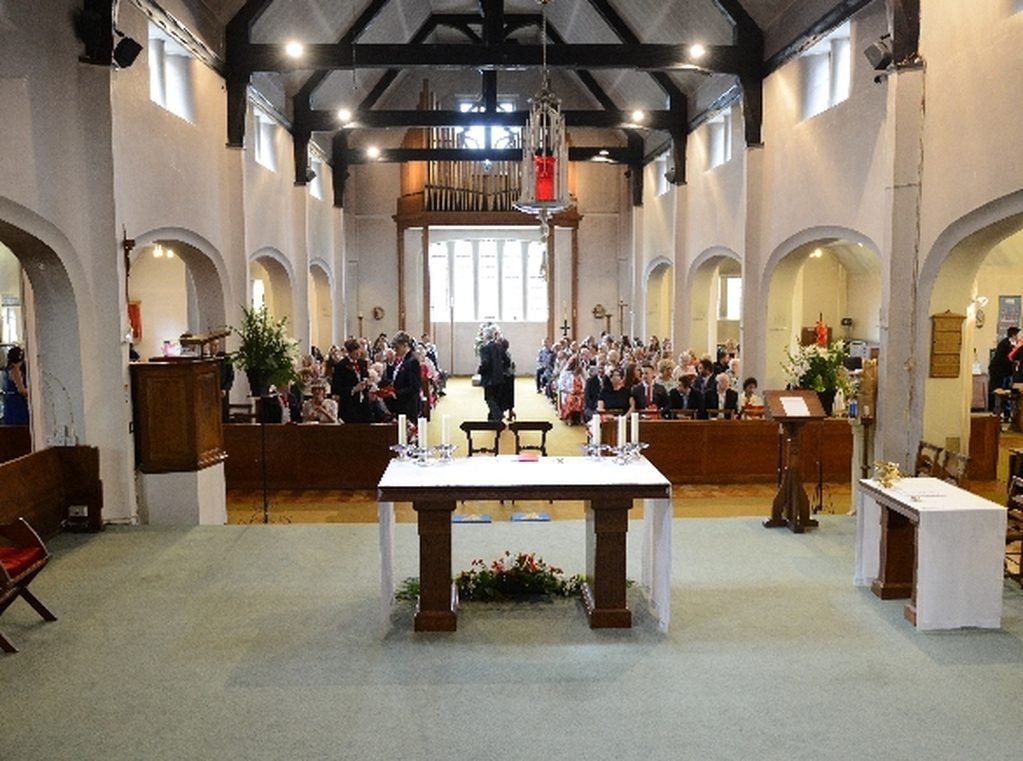 The interior of St John&rsquo;s during a service, looking west from the sanctuary across the nave altar to a full congregation.